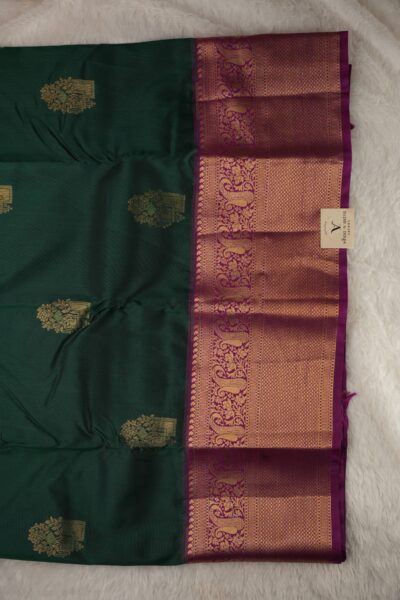 Close-up texture of the bottle green blended silk body showing woven gold buttis alongside the heavy, intricate gold zari peacock work of the magenta Kanchi border.