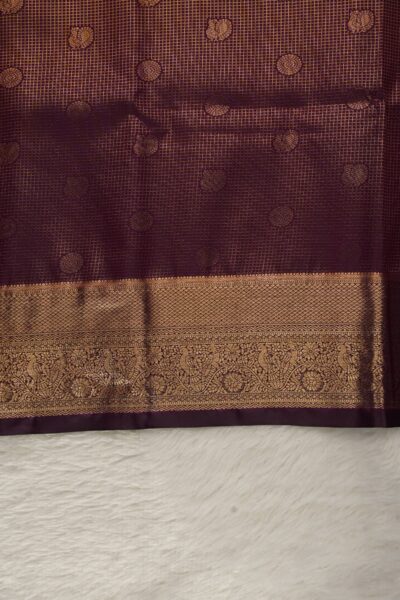 Close-up texture of the dark wine blended silk body showing the classic gold zari checks (kattam) alongside the heavy, intricate gold zari work of the Kanchi border.