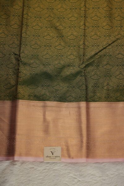 Close-up texture of the green blended silk body showing the dense, intricate gold zari floral network alongside the heavy, traditional gold zari elephant and peacock work of the baby pink Kanchi border.