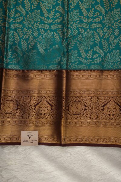 Close-up texture of the green blended silk body showing the elegant gold zari leaf weaving alongside the heavy, intricate gold zari work of the coffee brown Kanchi border.