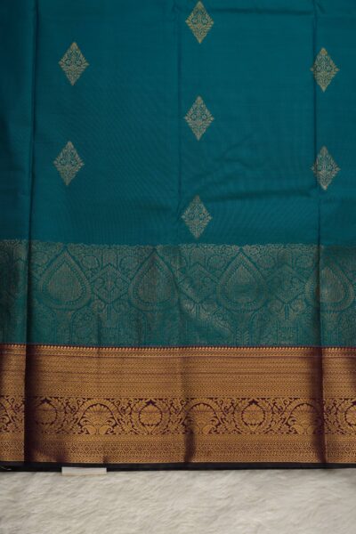 Close-up texture of the green blended silk body showing the dense, all-over gold zari weaving alongside the heavy, traditional gold zari peacock work of the magenta Kanchi border.