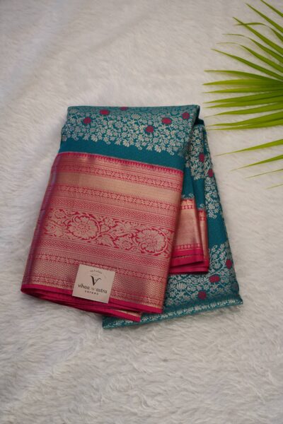 Close-up texture of the green blended silk body showing vertical gold zari lines alongside the heavy, intricate gold zari peacock work of the pink Kanchi border.