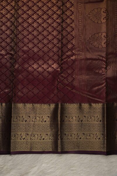 A detailed full view of the rich, dense gold zari geometric diamond brocade pallu woven on the burgundy base of the semi pattu silk saree.