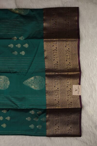 Close-up texture of the green blended silk body showing woven gold buttis alongside the heavy, intricate gold zari elephant and peacock work of the burgundy Kanchi border.