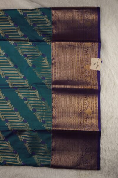 Close-up texture of the green blended silk body showing woven gold buttis alongside the heavy, intricate gold zari peacock work of the purple Kanchi border.