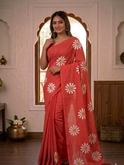 Smiling woman wearing a vibrant red khadi cotton saree with scattered white daisy floral prints and a matching pallu with red tassels.
