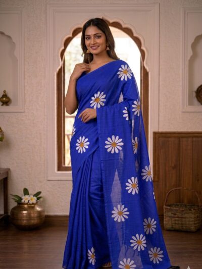 Smiling woman wearing a vibrant royal blue khadi cotton saree with scattered white daisy floral prints and a matching pallu with black tassels.