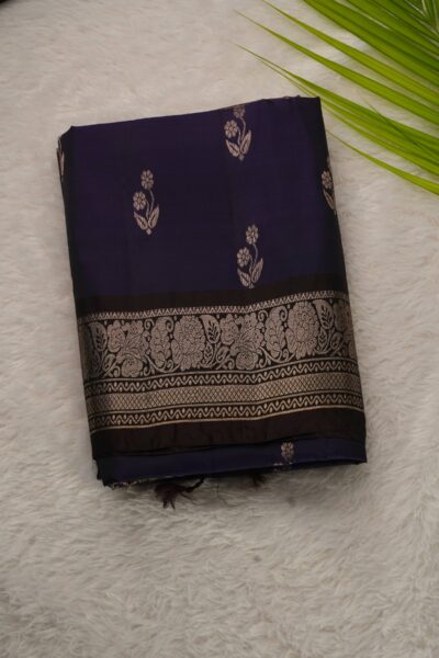 Folded navy blue lightweight Kanchi Pattu saree showcasing silver-tone floral buttis and a contrast coffee brown border with intricate floral zari vines.