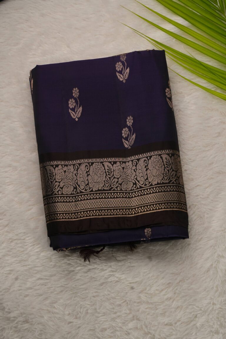 Folded navy blue lightweight Kanchi Pattu saree showcasing silver-tone floral buttis and a contrast coffee brown border with intricate floral zari vines.