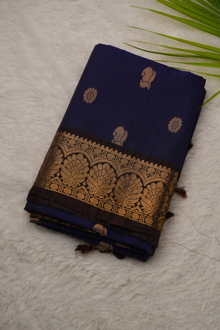 Folded navy blue lightweight Kanchi Pattu saree showcasing gold zari floral and paisley buttis and a contrast snuff brown border with intricate arch motifs.
