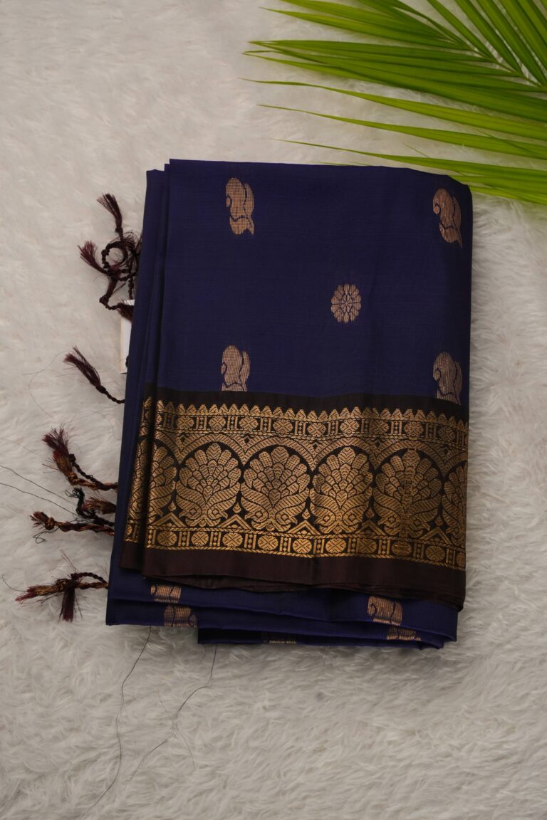 Folded navy blue lightweight Pattu saree showcasing gold zari floral and paisley buttis and a contrast coffee brown border with intricate leaf arch motifs.