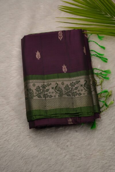 Folded magenta lightweight Pattu saree showcasing metallic floral buttis, paired with a vibrant light green contrast border featuring woven peacocks and green tassels.