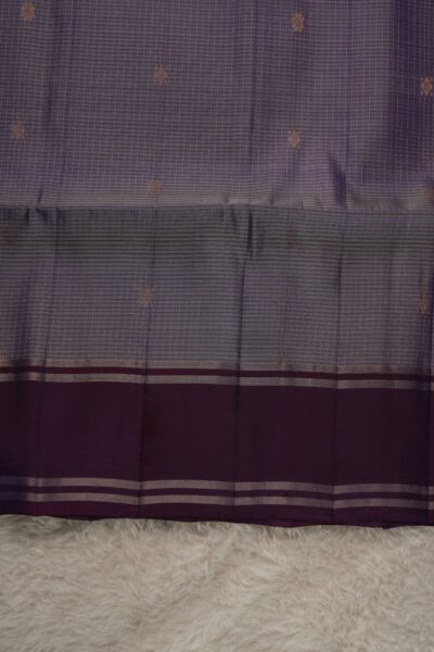 Close-up texture of a light lavender lightweight Pattu saree with woven checks and floral buttis, alongside a sleek deep magenta gap border with zari lines.