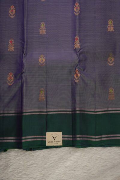 Close-up texture of a lavender lightweight Pattu saree with detailed red and green Meenakari floral buttis, alongside a sleek bottle green gap border with metallic lines.