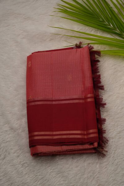 Folded peach lightweight Pattu saree showcasing fine zari checks, small floral buttis, and a contrast deep red gap border framed by metallic stripes.