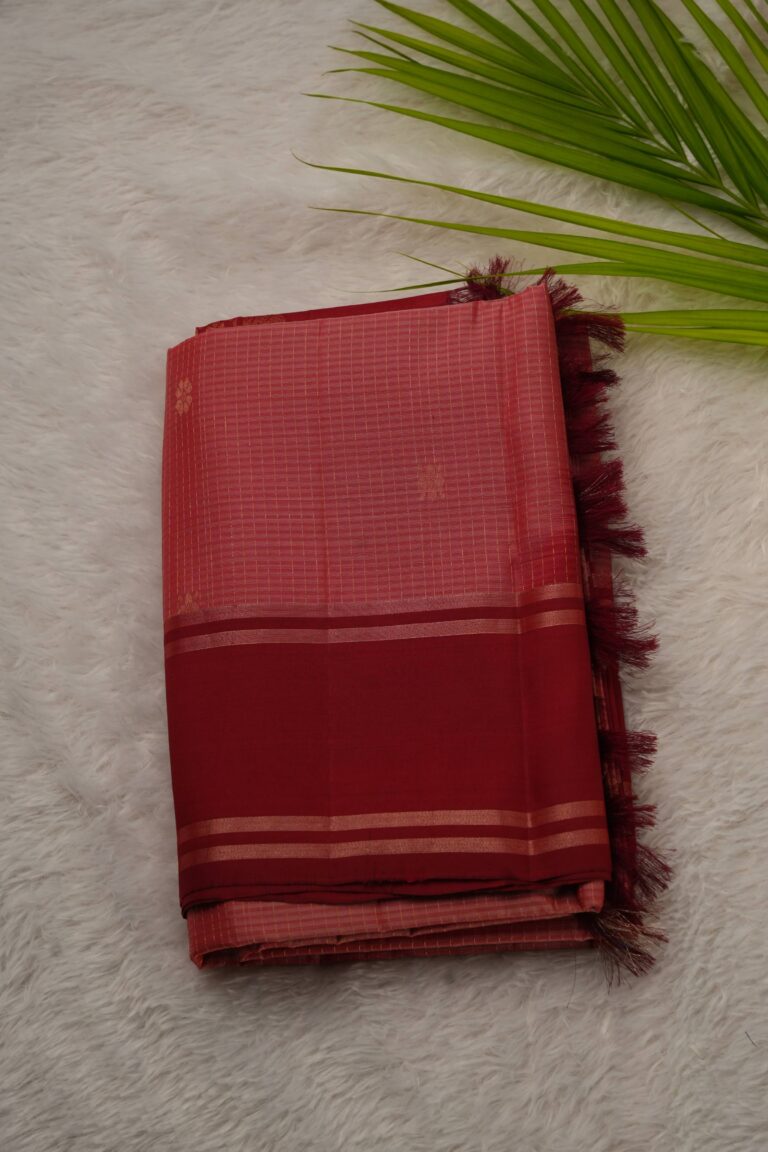 Folded peach lightweight Pattu saree showcasing fine zari checks, small floral buttis, and a contrast deep red gap border framed by metallic stripes.