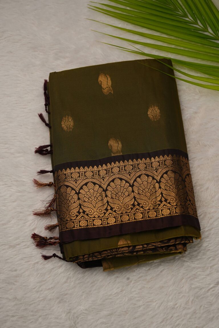 Folded olive green lightweight Pattu saree showcasing gold zari floral and paisley buttis and a contrast coffee brown border with intricate leaf arch motifs.
