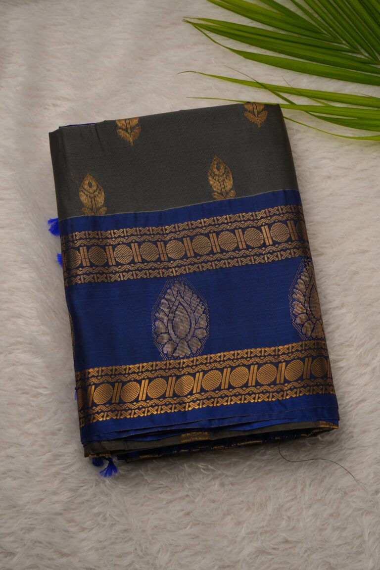Folded dark olive green lightweight Pattu saree showcasing gold zari leaf buttis and a contrast royal blue border with intricate geometric and large leaf motifs.