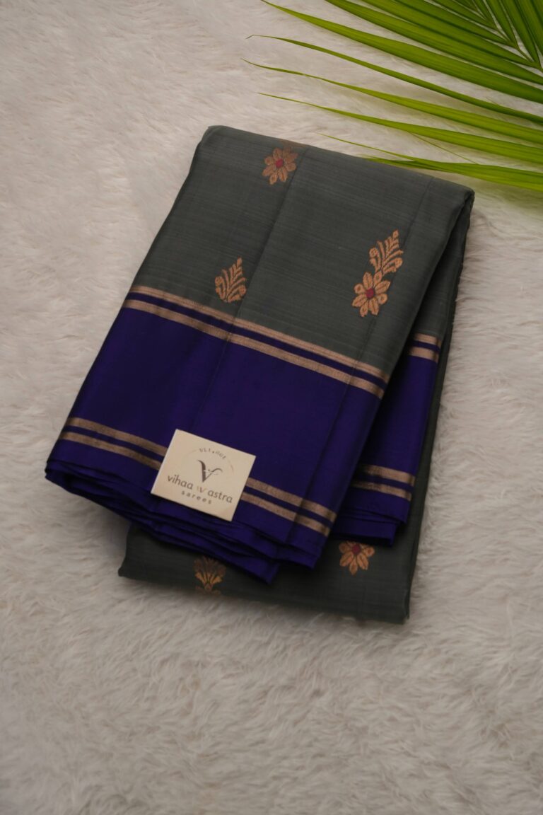 Folded charcoal-grey lightweight Pattu saree showcasing gold zari floral buttis and a contrast navy blue gap border framed by zari stripes.
