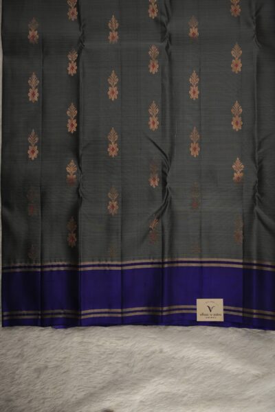 Close-up texture of a grey lightweight Pattu saree with gold and red floral buttis, alongside a sleek navy blue gap border with gold zari lines.