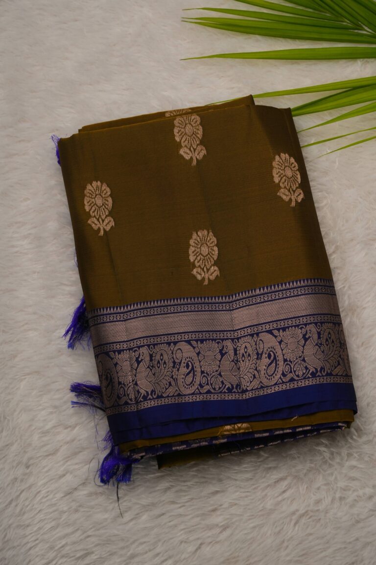 Folded earthy mustard lightweight Pattu saree showcasing large gold zari floral buttis and a contrast deep blue border with intricate peacock motifs.