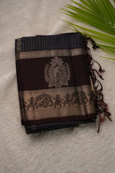 Folded navy blue lightweight Kanchi Pattu saree showcasing fine zari checks, large stylized border motifs, and a beautiful palanquin procession band on a coffee brown gap border.