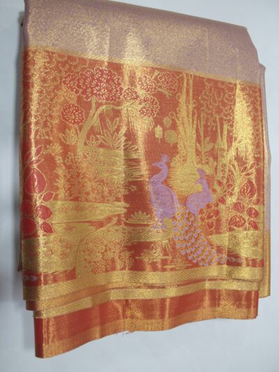 Folded elegant Semi Kanchi Pattu saree showcasing a soft shimmering body and a heavy copper-gold zari pallu woven with detailed trees and peacock motifs featuring purple Meenakari accents.