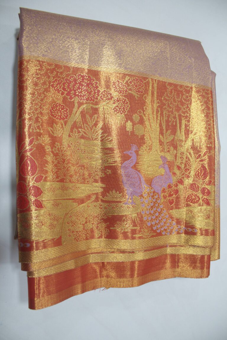Folded elegant Semi Kanchi Pattu saree showcasing a soft shimmering body and a heavy copper-gold zari pallu woven with detailed trees and peacock motifs featuring purple Meenakari accents.