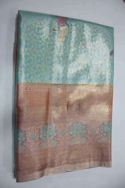 Folded Aqua Green Semi Kanchi Pattu saree showcasing all-over gold zari floral brocade, a Meenakari peacock motif, and a heavy metallic mauve-copper border with green floral tree meenakari patterns.