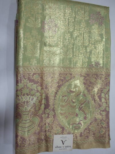Folded Pista Green Semi Kanchi Pattu saree showing an all-over gold zari botanical brocade and a heavy metallic mauve border with a large peacock paisley and floral vase motif accented with Meenakari weaving.