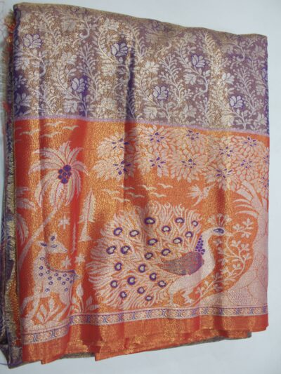 Folded purple Semi Kanchi Pattu saree with floral zari brocade, paired with a vibrant orange pallu displaying a beautifully woven scenic landscape featuring a grand peacock, deer, and trees with blue Meenakari accents.