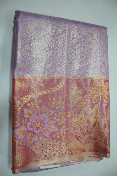 Folded lavender Semi Kanchi Pattu saree showing an all-over gold zari botanical brocade and a heavy contrasting rose-red border featuring a woven landscape with palm trees, a sun, and a large floral motif accented with purple Meenakari weaving.
