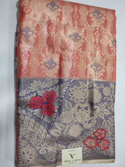 Folded red Semi Kanchi Pattu saree showcasing an all-over gold zari floral brocade with blue accents, and a heavy contrasting navy blue border featuring large floral motifs accented with bright red Meenakari weaving.