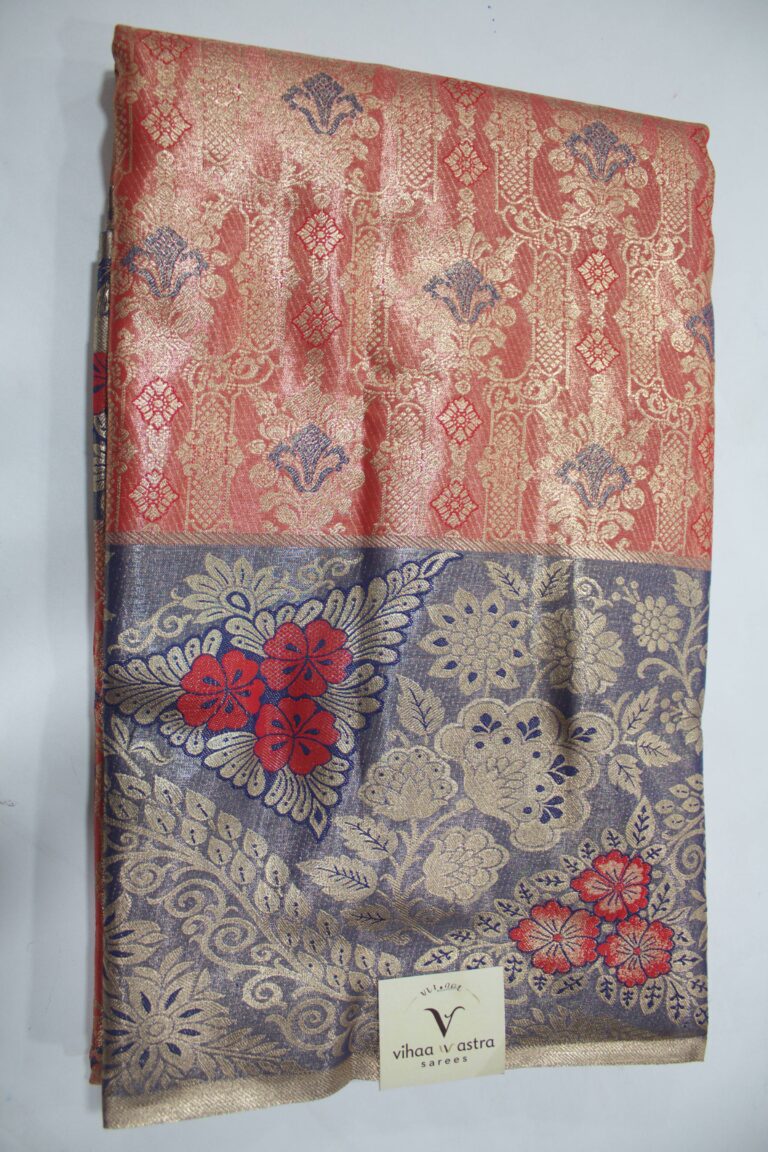 Folded red Semi Kanchi Pattu saree showcasing an all-over gold zari floral brocade with blue accents, and a heavy contrasting navy blue border featuring large floral motifs accented with bright red Meenakari weaving.