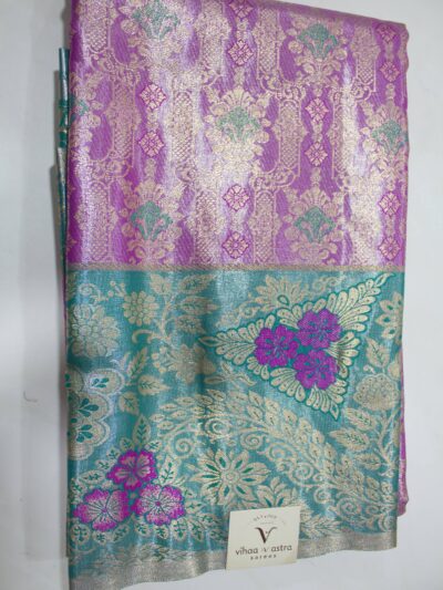 Folded violet Semi Kanchi Pattu saree showcasing an all-over gold zari floral brocade with green accents, and a heavy contrasting teal border featuring large floral motifs accented with bright violet Meenakari weaving.