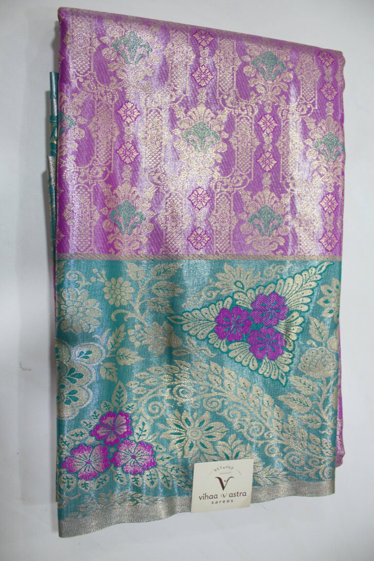 Folded violet Semi Kanchi Pattu saree showcasing an all-over gold zari floral brocade with green accents, and a heavy contrasting teal border featuring large floral motifs accented with bright violet Meenakari weaving.