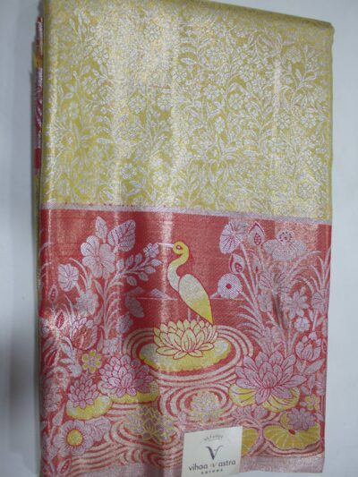 Folded yellow Semi Kanchi Pattu saree showing an all-over zari botanical brocade and a heavy contrasting coral-red border featuring a woven landscape of a swan in a lotus pond accented with yellow Meenakari weaving.