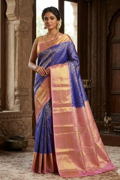 Beautiful woman wearing a royal blue premium Kanjeevaram Pattu saree featuring a contrast baby pink heavy gold zari pallu and all-over body motifs.