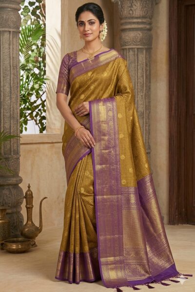 Beautiful woman wearing a golden yellow premium semi Kanchi Pattu saree featuring gold zari checks and a contrasting purple heavy zari pallu with tassels.