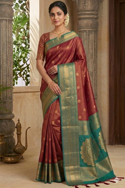 Beautiful woman wearing a deep red premium semi Kanchi Pattu saree featuring gold zari checks and a contrasting green heavy zari pallu with large floral mandala motifs.