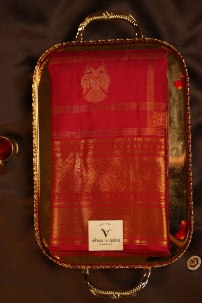 Beautifully folded self red pure handloom Kanjeevaram saree on a brass tray, highlighting the vintage zari checks and traditional gold border.