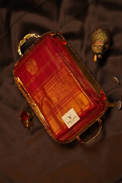 Another angled view of the folded red pure handloom Kanjeevaram saree resting on a decorative tray next to a brass elephant showpiece.