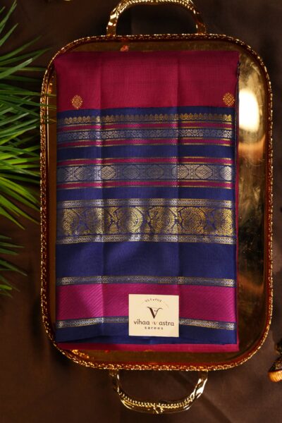 Neatly folded pink pure handloom Kanjeevaram Pattu saree showcasing the vibrant body with gold buttis and the contrasting vintage blue gap border.