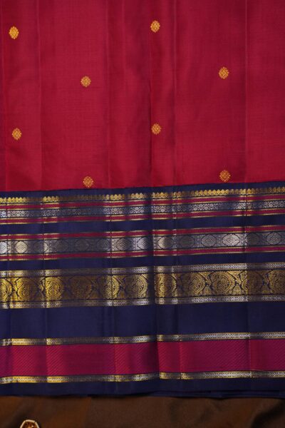 Close-up texture of the pure handloom pink silk body showing woven gold chakra buttis alongside the rich horizontal zari stripes of the blue border.
