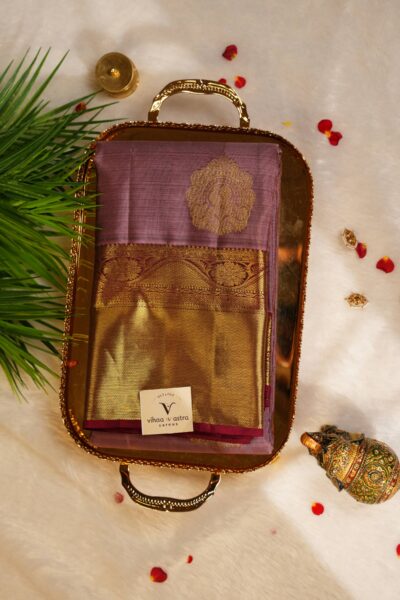 Beautifully folded rose pink pure handloom Kanjeevaram Pattu saree resting on a decorative brass tray, showcasing the delicate gold buttis and heavy maroon border.