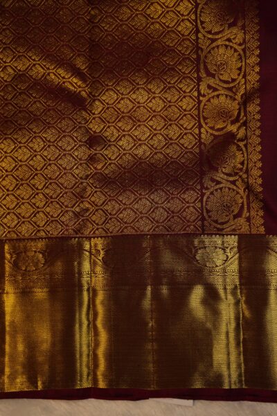Close-up highlighting the intricate transition between the geometric diamond brocade pallu and the traditional peacock motifs on the maroon border.