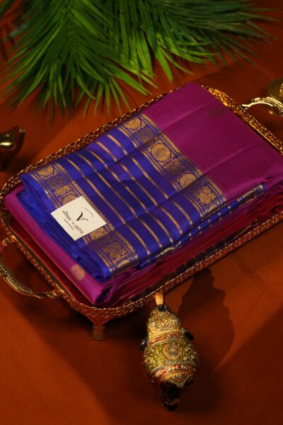 Beautifully draped outlook of the pure handloom Kanjeevaram pattu saree in pink and blue, resting on a decorative tray next to traditional Indian elements.