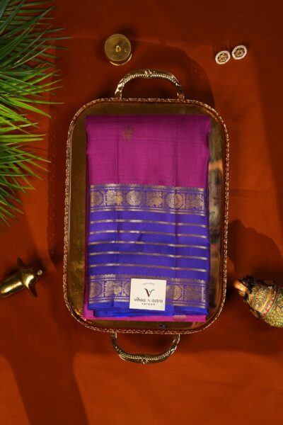 Beautifully draped outlook of the pure handloom Kanjeevaram pattu saree in pink and blue, resting on a decorative tray next to traditional Indian elements.