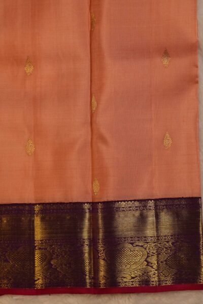 Close-up texture of the pure handloom peach silk body showing woven gold chakra buttis alongside the rich horizontal zari stripes of the magenta border.