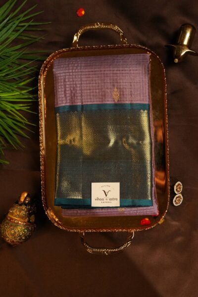 Top view of the beautifully folded warm peach pure handloom Kanjeevaram Pattu saree resting on a decorative brass tray, showcasing the delicate gold stripes and heavy navy blue border.